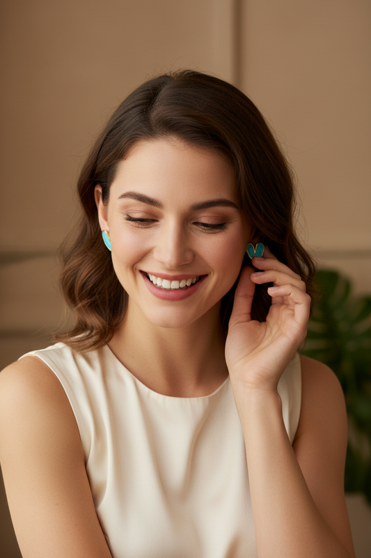 Turquoise heart-shaped earrings with gold accents on a white surface with yellow flowers in the background.
